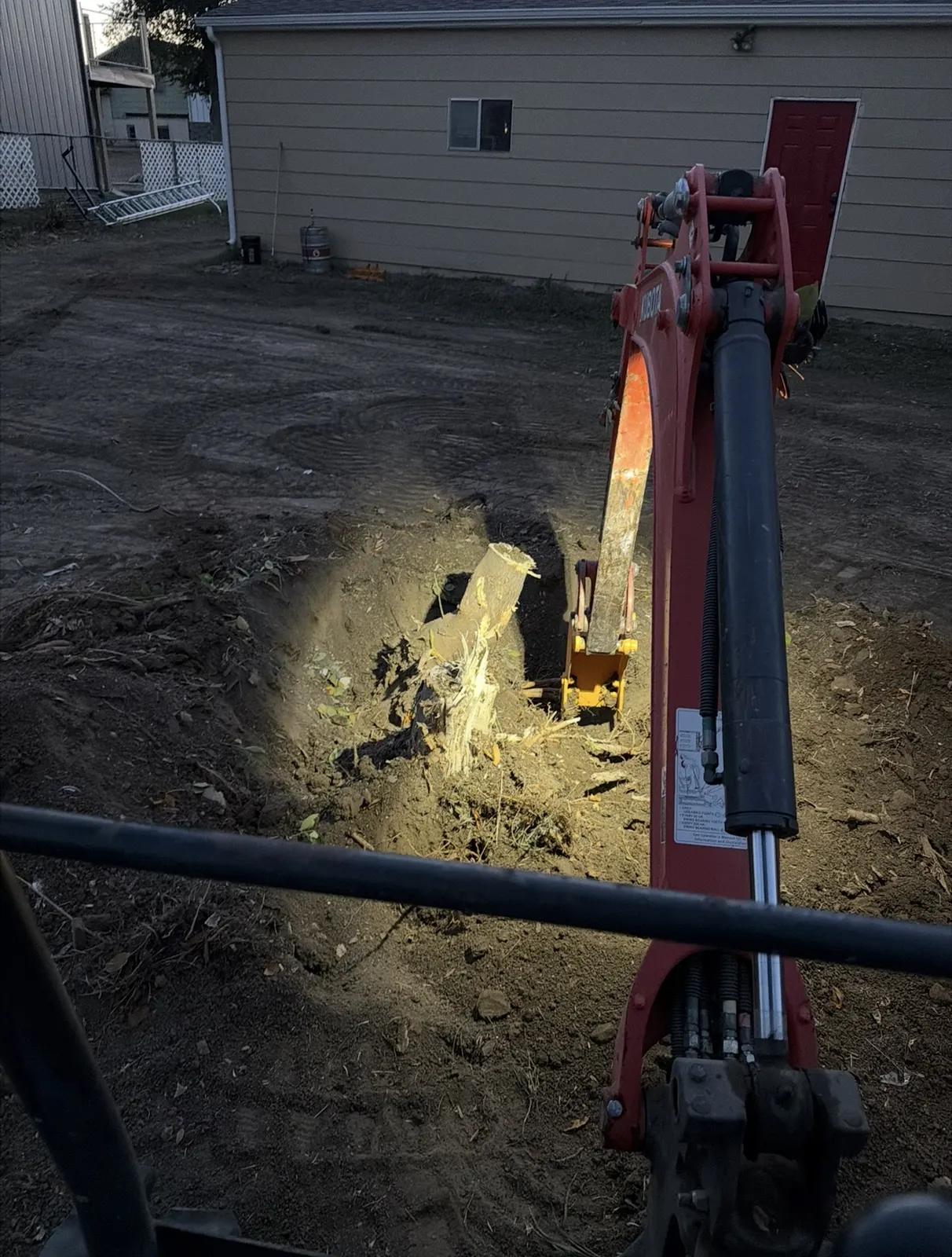 Mini excavator working a stump out of a backyard under work lights
