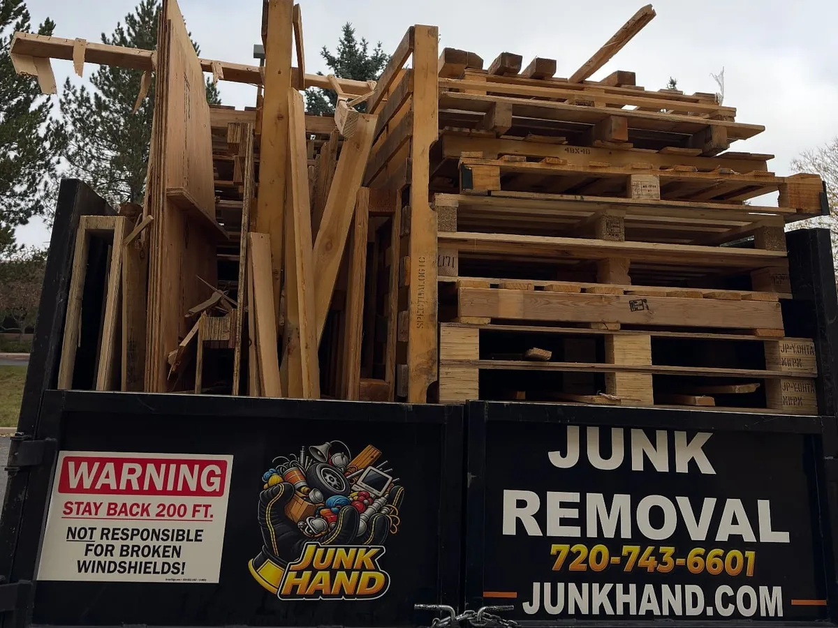 Junk Hand junk removal dump truck with branded tailgate carrying a full load of wooden pallets and scrap lumber out of a Boulder commercial pallet pickup