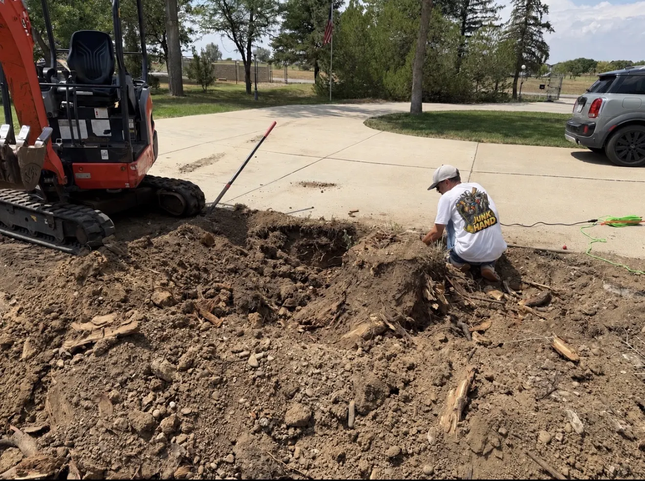 Junk Hand crew member cutting roots next to a mini excavator during stump removal